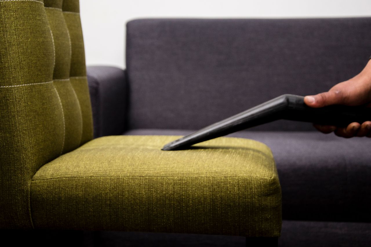 Gros plan d’une personne passant l’aspirateur sur un fauteuil de salon moderne en intérieur, mettant en valeur un service de nettoyage.